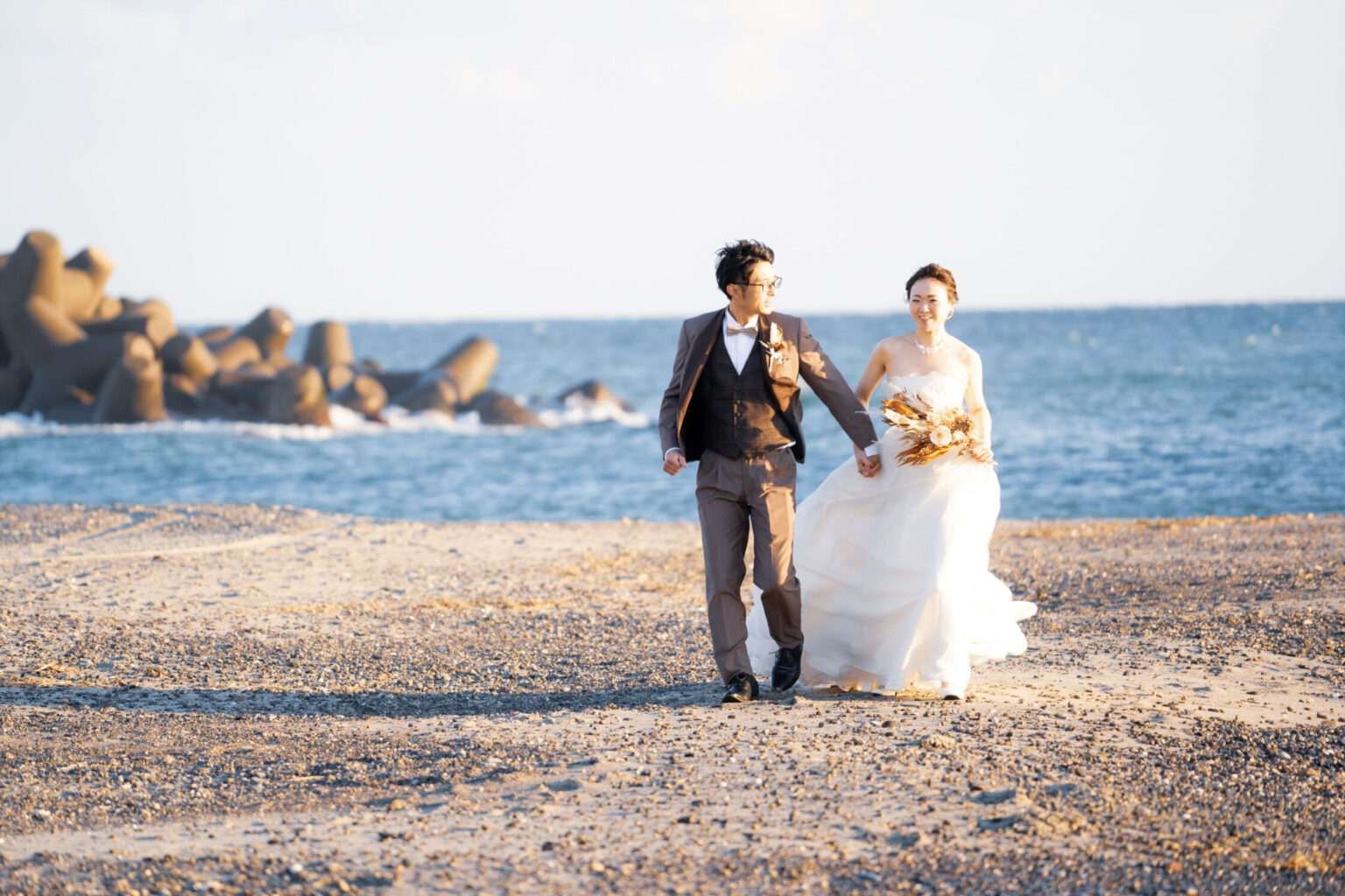 海辺の砂浜を歩く新郎新婦