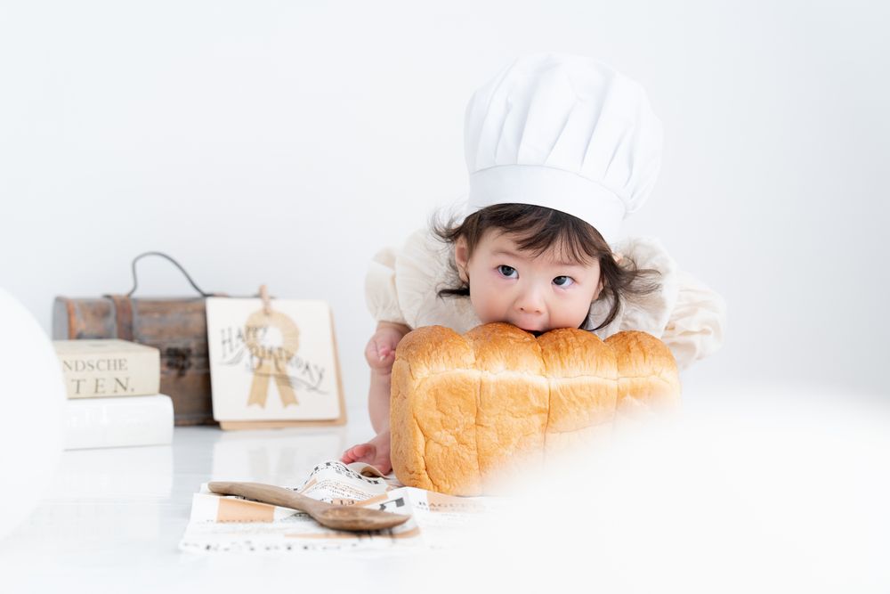 コック帽をかぶって食パンにかぶりつく赤ちゃん