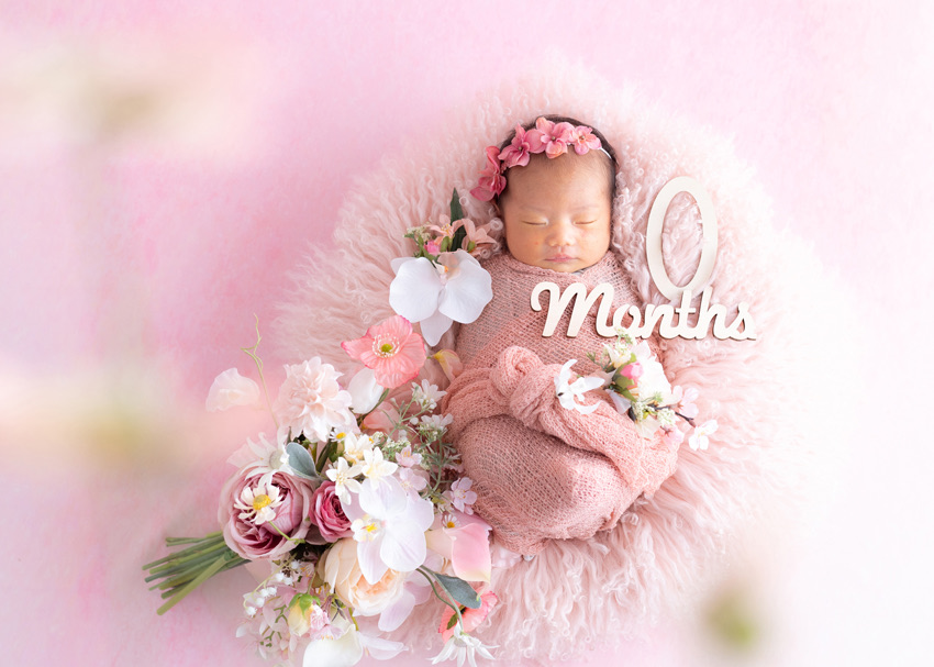 0monthsのレターとピンクの花に囲まれて眠る新生児