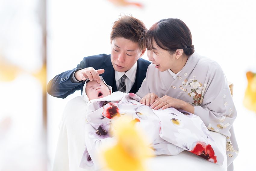 晴れ着の赤ちゃんをのぞきこんで笑顔になるパパとママ