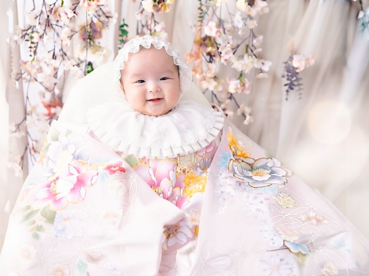 桜のセットで淡い色の晴れ着に包まれて笑う赤ちゃん