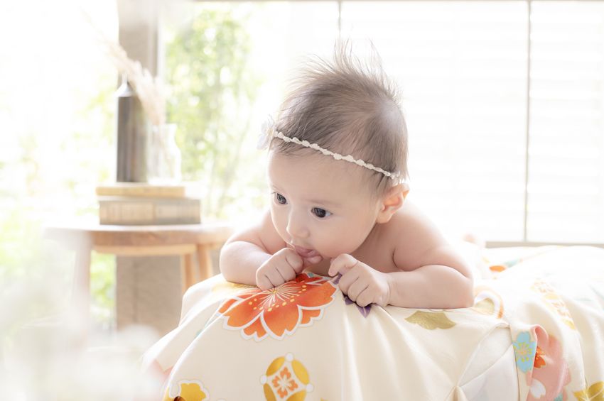 ヘアバンドをつけてうつ伏せで顔を上げる百日祝いの赤ちゃん