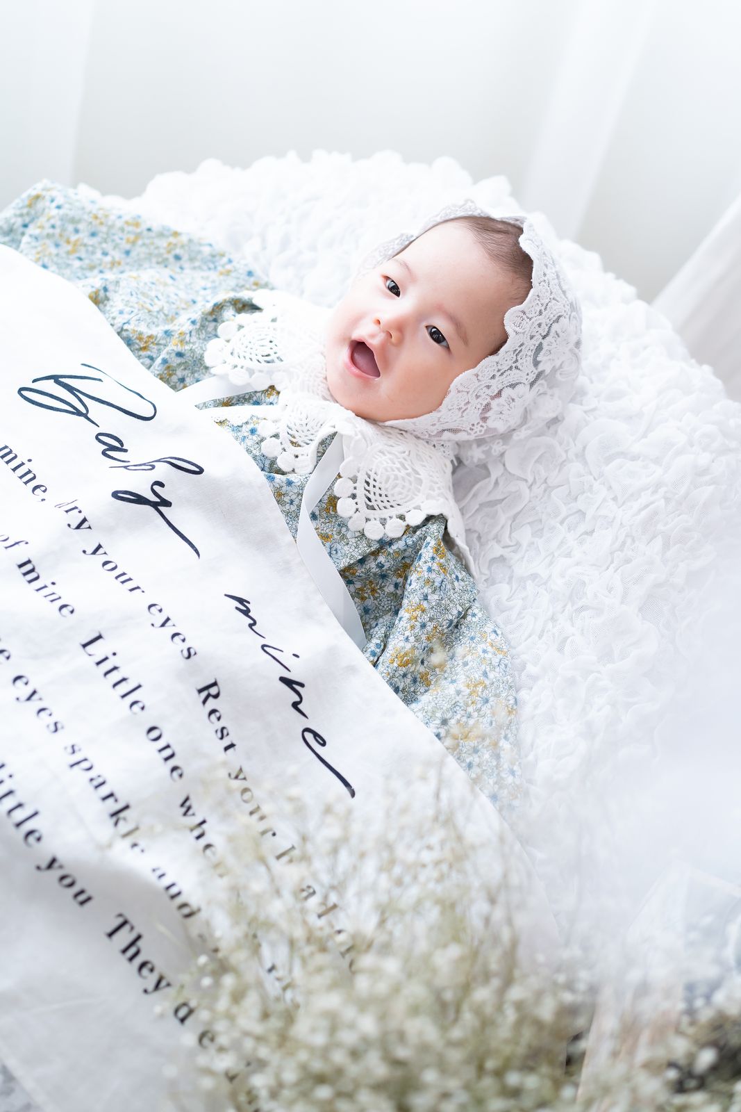 Baby mineのブランケットとレースのボンネットで笑うお宮参りの赤ちゃん