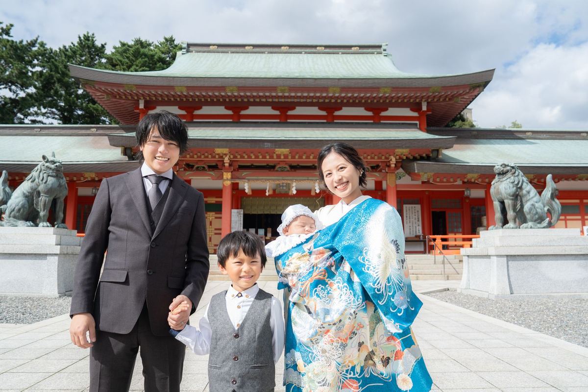 神社の前で晴れ着の赤ちゃんを抱く家族