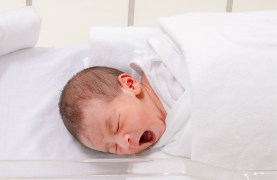 院内のベッドであくびをする新生児