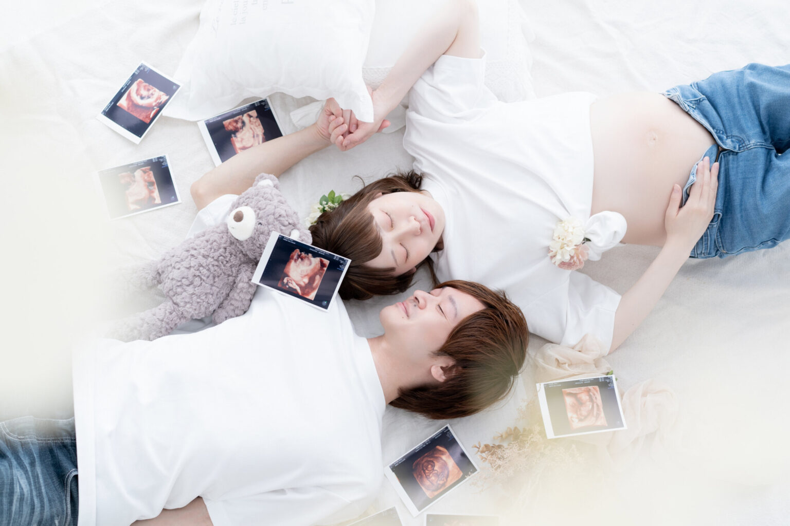 エコー写真に囲まれて寝転ぶ夫婦のマタニティフォト