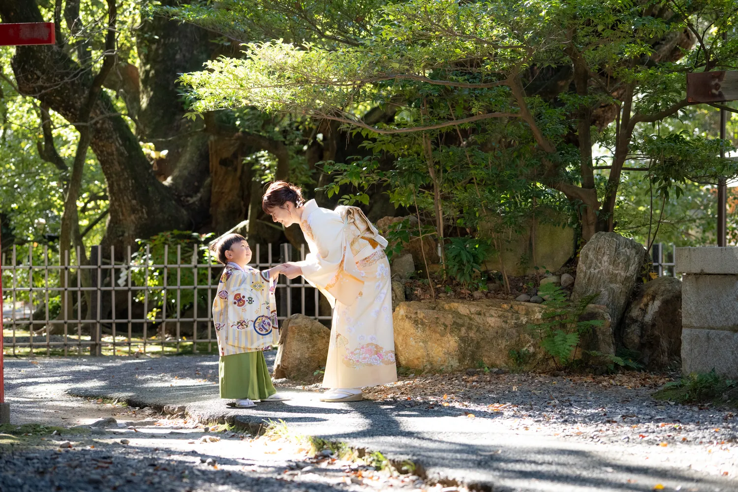 神社の木陰で七五三の男の子に寄り添うお母さん