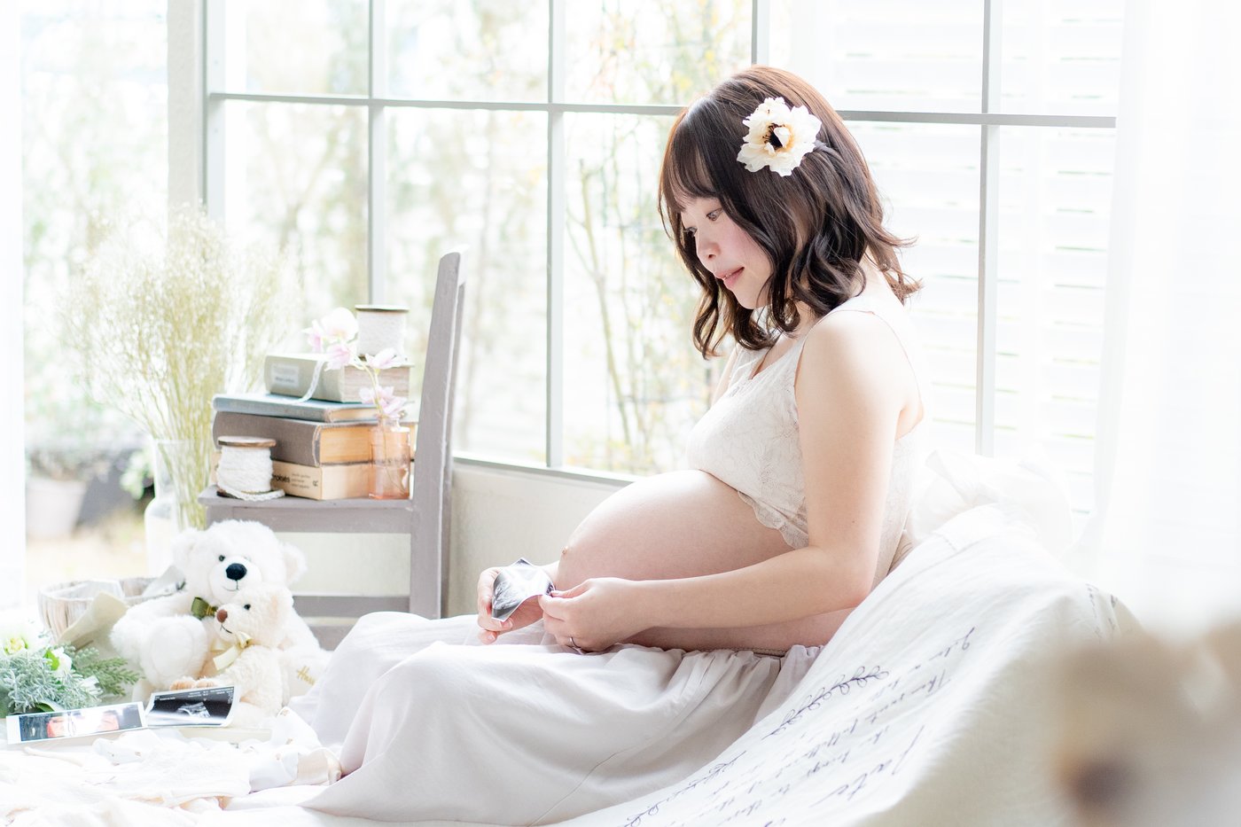 窓辺でお腹に手をあてる妊婦さんのマタニティフォト