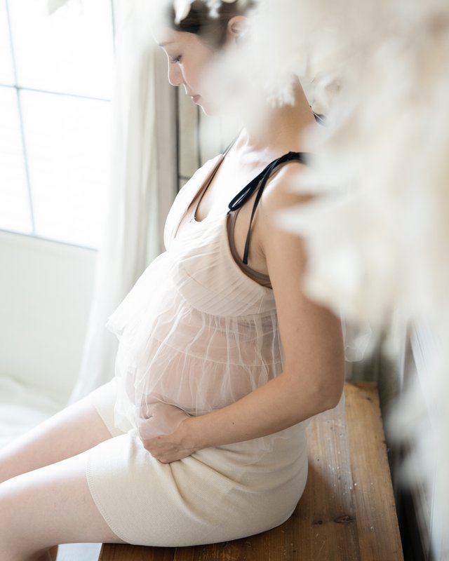 窓辺に座りお腹に手をあてる妊婦さん