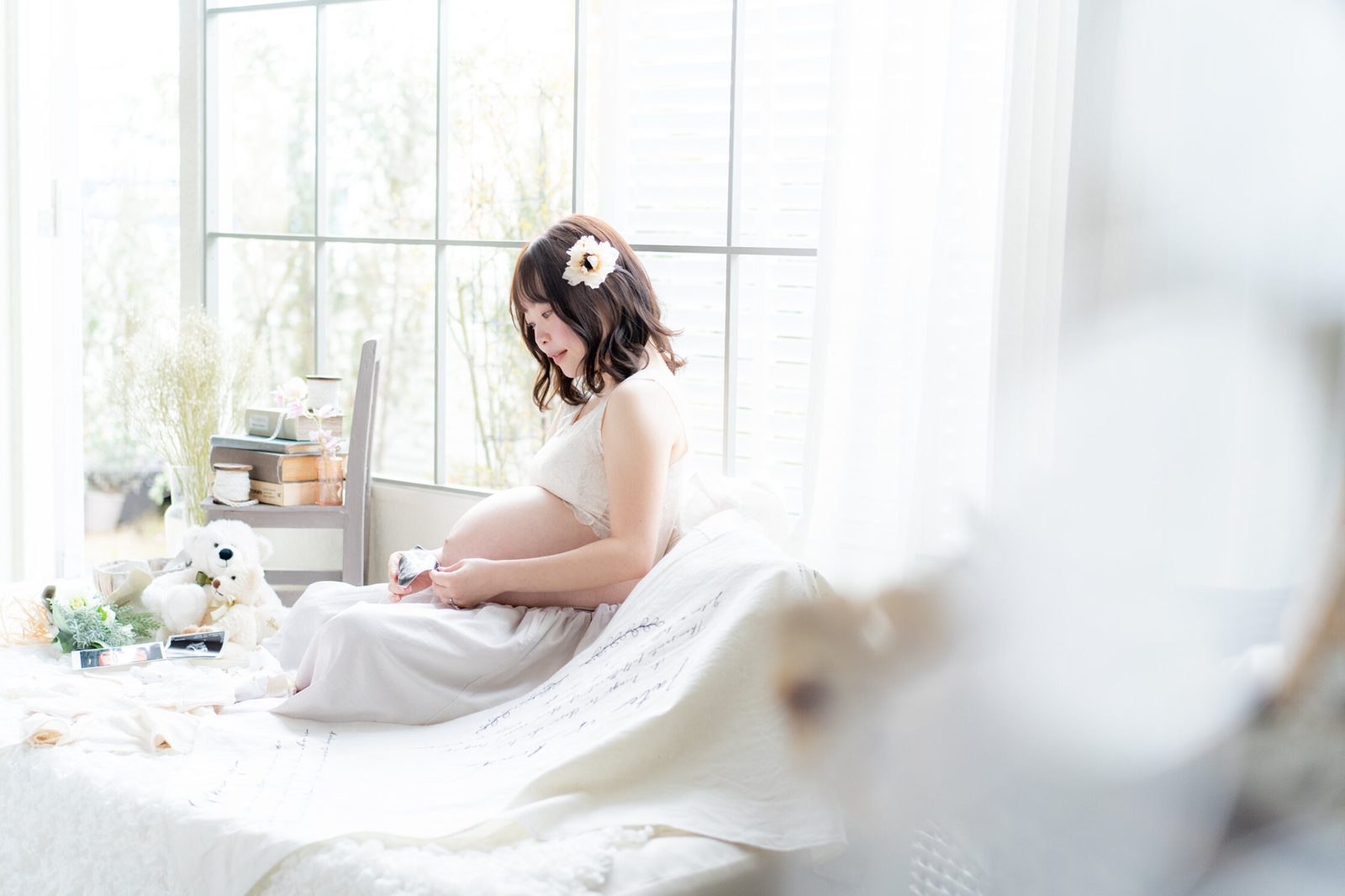 窓辺でお腹に手をあてる妊婦さんのマタニティフォト