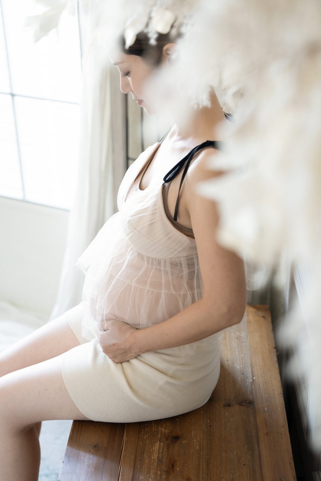 窓辺の椅子に座りお腹に手をあてる妊婦さん